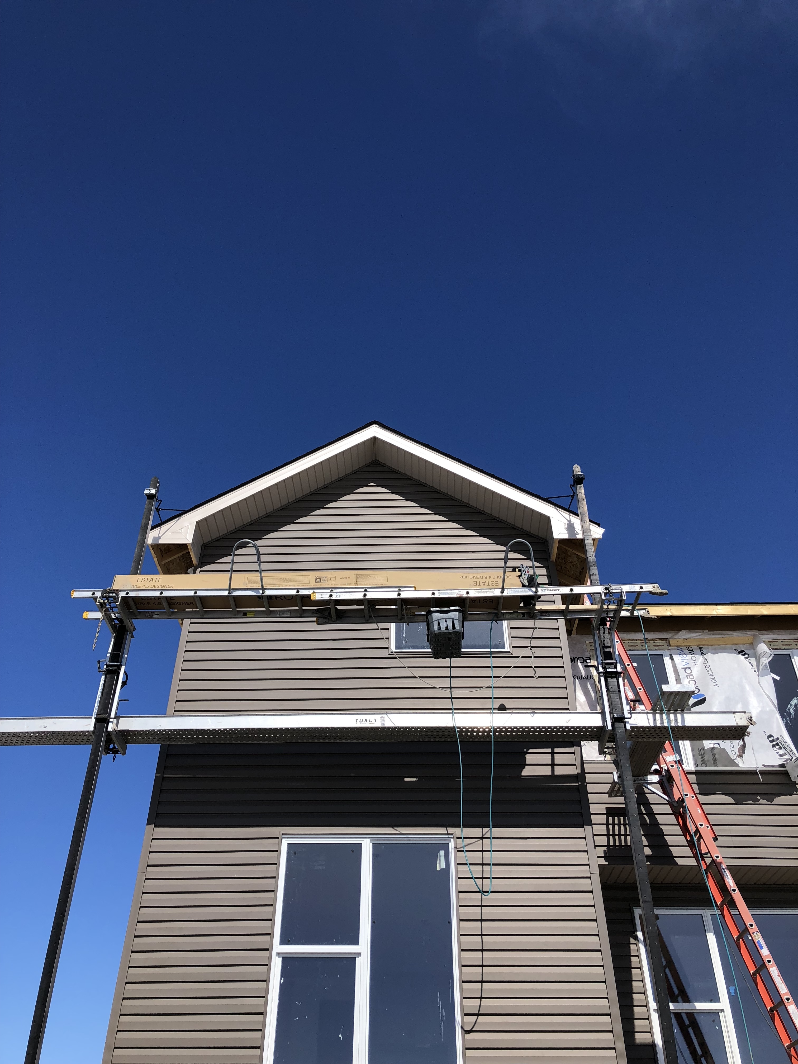 Exterior residential construction with scaffold and ladder against a house under clear blue sky.